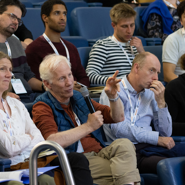 Main image of attendees asking questions from their seats with microphone. Secondary image is of group of attendees in a lecture hall clapping.
