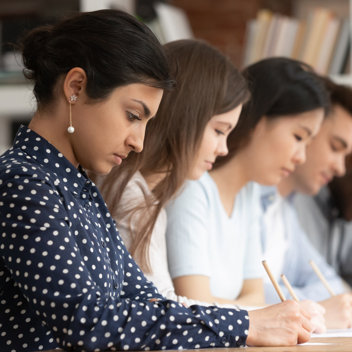 Main image of a group of diverse students sitting in a row, focused on writing during a classroom activity. Secondary image is of attendees in a room discussing research on poster boards.