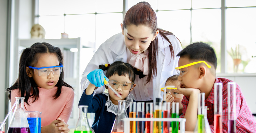 Female teacher showing three young children how to conduct a science experiment