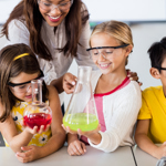 Teacher helping pupils with science experiment involving colourful liquids in flasks