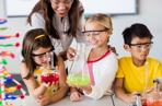 Teacher helping pupils with science experiment involving colourful liquids in flasks