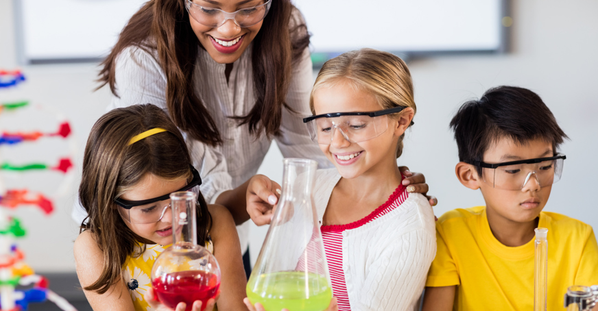 Teacher helping pupils with science experiment involving colourful liquids in flasks