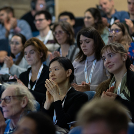 Main image Group of people exploring interactive displays in a modern, well-lit exhibition space with white walls and ceiling panels. Secondary image is group of audience members in a lecture hall clapping.