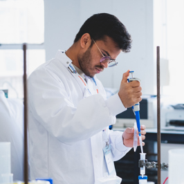 Main image of scientists in white lab coats and green gloves conducting experiments with lab equipment on a cluttered table in a busy laboratory. Secondary image is of group of attendees in a room with poster boards on display.