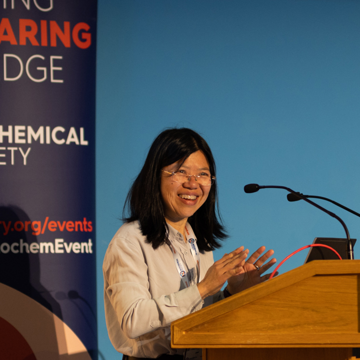 Main image of female speaker in front of a wooden podium and Biochemical Society banner backdrop. Secondary image is of group of attendees networking among poster boards.