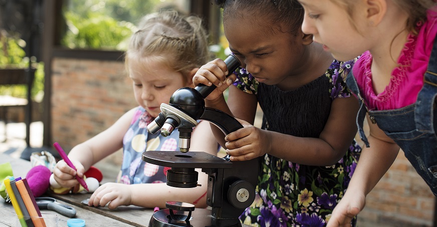 three young children looking through a microscope