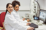 Two students in a lab using a microscope and computer