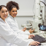 Two students in a lab using a microscope and computer