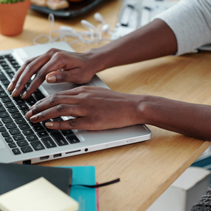Photograph of hands typing on a laptop.