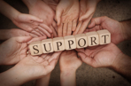 Group of hands holding wooden blocks spelling out support
