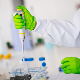 Main image is of two researchers with their laptops on a chair in discussion. Secondary image is of scientist wearing green gloves using a pipette to transfer liquid in a laboratory setting.